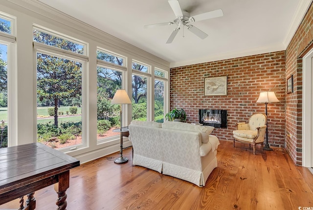 living room with a brick fireplace, ceiling fan, light wood-type flooring, brick wall, and ornamental molding