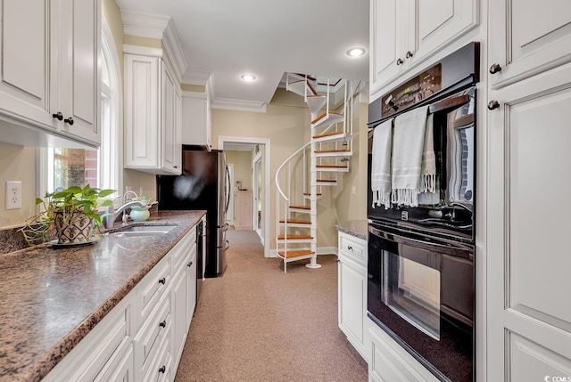 kitchen with a sink, stainless steel appliances, white cabinetry, light colored carpet, and crown molding