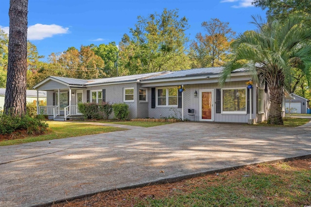 ranch-style home with concrete driveway, a porch, metal roof, and brick siding