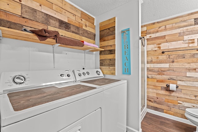 clothes washing area with independent washer and dryer, wood walls, a textured ceiling, wood finished floors, and baseboards