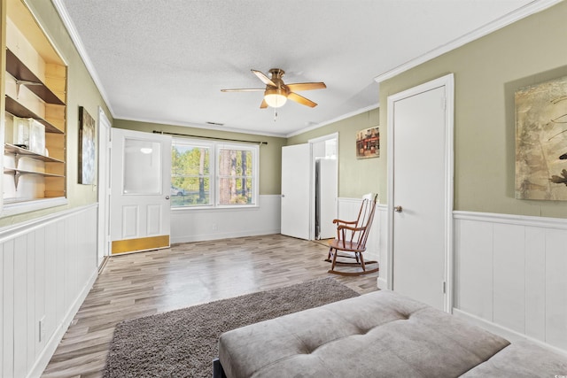 living area featuring crown molding, wood finished floors, a ceiling fan, wainscoting, and a textured ceiling