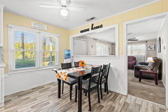 dining room with a ceiling fan, a textured ceiling, light wood-style floors, ornamental molding, and a decorative wall