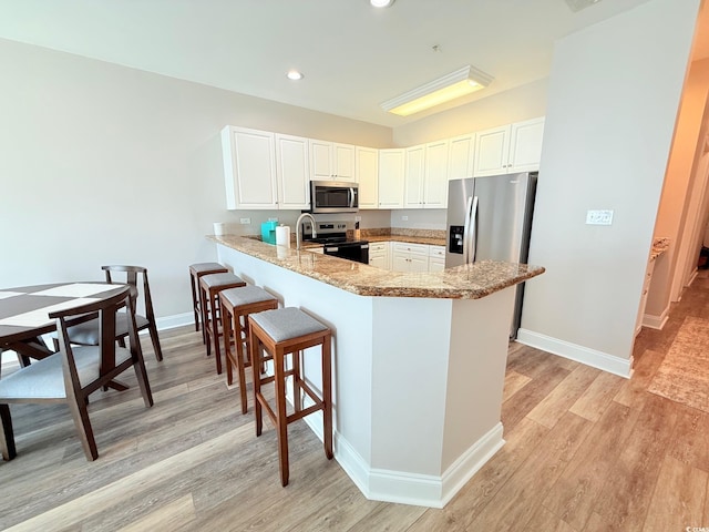 1025 World Tour Blvd Unit 205, Myrtle Beach, SC 29579 - kitchen with stainless steel appliances, baseboards, a peninsula, light wood-style flooring, and white cabinetry