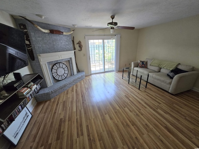 living room with a ceiling fan, a textured ceiling, wood finished floors, and a fireplace