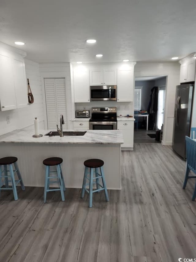 725 Juniper Dr, Surfside Beach, SC 29575 - kitchen with appliances with stainless steel finishes, a sink, a breakfast bar, white cabinets, and a peninsula