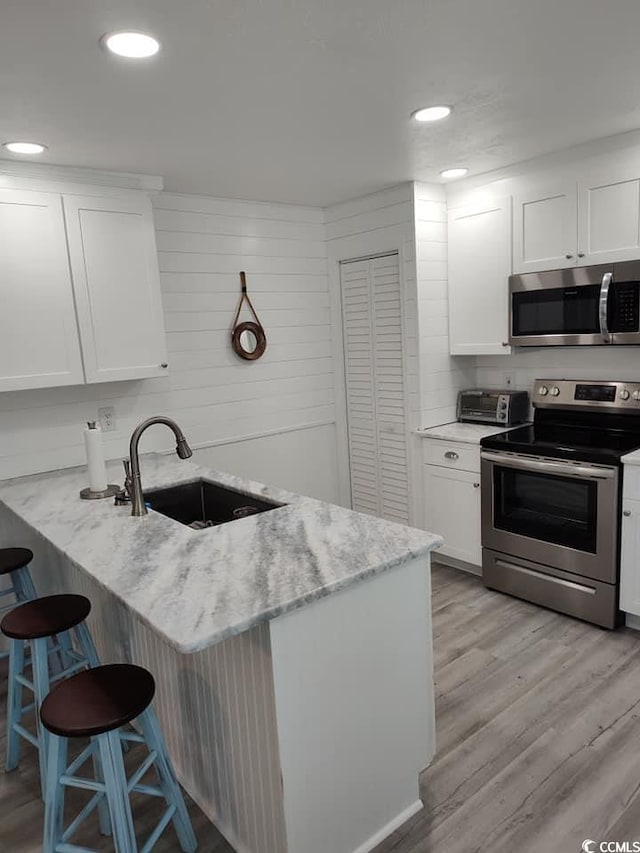 725 Juniper Dr, Surfside Beach, SC 29575 - kitchen with stainless steel appliances, a sink, a breakfast bar area, white cabinets, and a peninsula