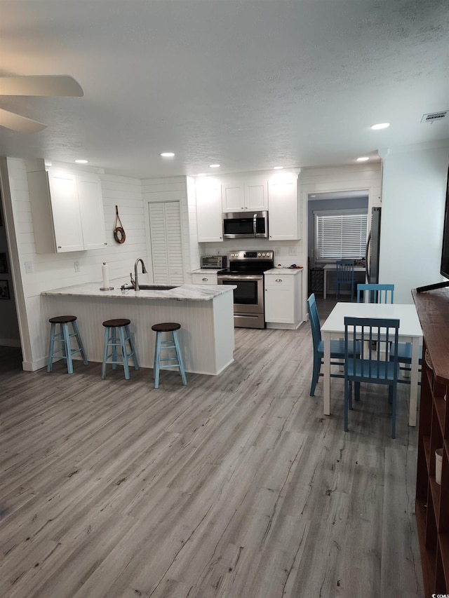 725 Juniper Dr, Surfside Beach, SC 29575 - kitchen with stainless steel appliances, a sink, a peninsula, white cabinets, and a kitchen breakfast bar