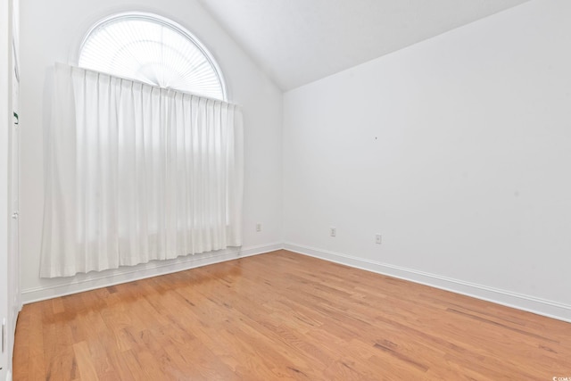spare room with lofted ceiling, baseboards, and light wood finished floors