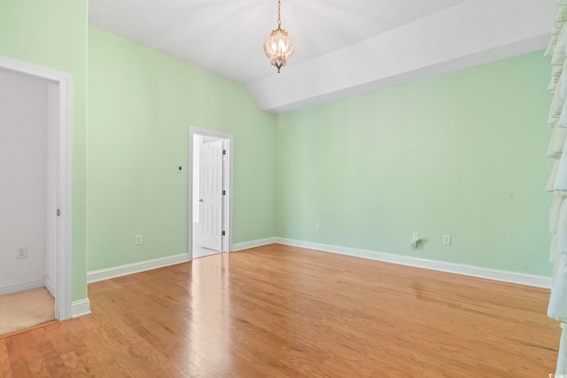 spare room featuring light wood-type flooring, baseboards, an inviting chandelier, and lofted ceiling