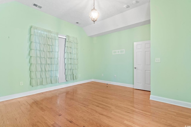 spare room featuring baseboards, vaulted ceiling, visible vents, and light wood-type flooring