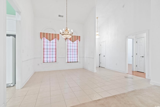 unfurnished dining area featuring tile patterned floors, baseboards, an inviting chandelier, visible vents, and a high ceiling