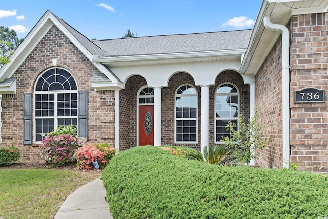 property entrance featuring roof with shingles and brick siding