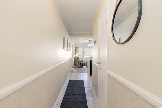 hallway featuring baseboards, a textured ceiling, ornamental molding, and light tile patterned flooring
