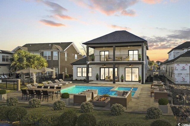 1219 Bentcreek Ln, Myrtle Beach, SC 29579 - back of property at dusk featuring ceiling fan, a balcony, an outdoor living space with a fire pit, a patio area, and an outdoor pool