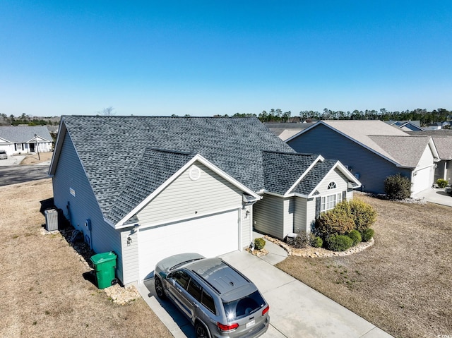 view of front facade featuring roof with shingles, a garage, cooling unit, concrete driveway, and a residential view
