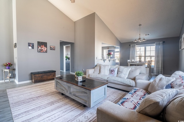 living room with a chandelier, light wood-type flooring, high vaulted ceiling, and baseboards