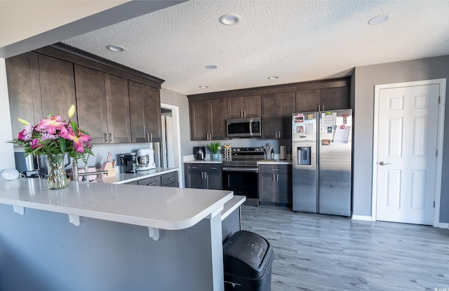kitchen featuring appliances with stainless steel finishes, dark brown cabinetry, a textured ceiling, light countertops, and light wood-style flooring
