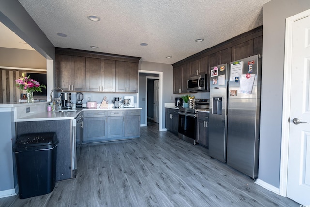 kitchen with stainless steel appliances, a sink, light wood finished floors, light countertops, and dark brown cabinetry