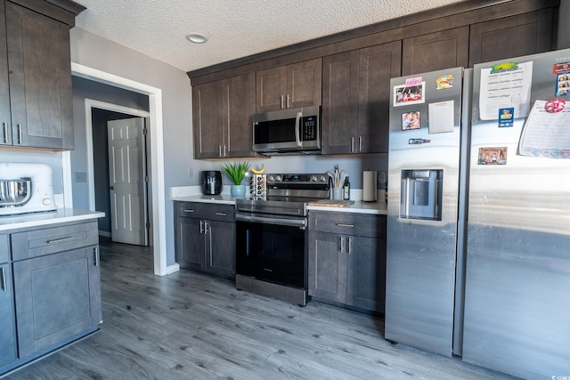 kitchen with appliances with stainless steel finishes, light countertops, dark brown cabinets, light wood-style flooring, and a textured ceiling