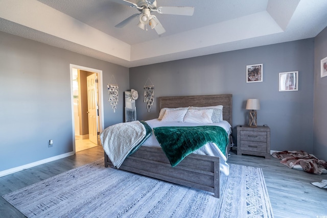 bedroom featuring a raised ceiling, wood finished floors, baseboards, and ceiling fan