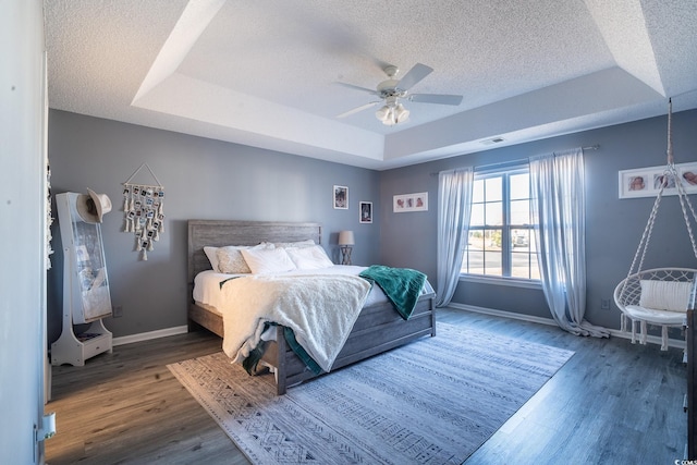 bedroom featuring a tray ceiling, baseboards, a textured ceiling, wood finished floors, and ceiling fan