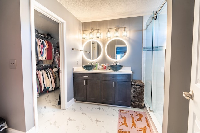 full bath featuring a stall shower, marble look tiles, a textured ceiling, a spacious closet, and double vanity