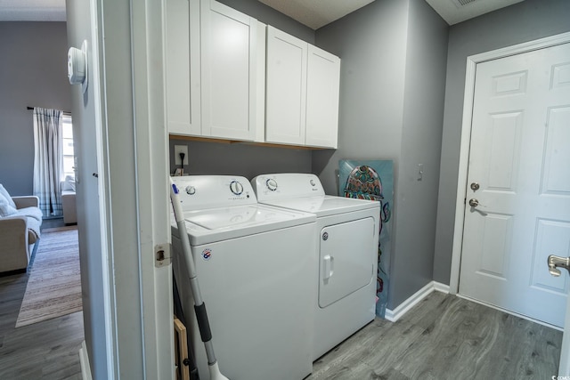 washroom featuring washing machine and clothes dryer, wood finished floors, cabinet space, and baseboards