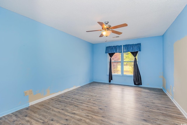 empty room with a textured ceiling, visible vents, baseboards, wood finished floors, and a ceiling fan
