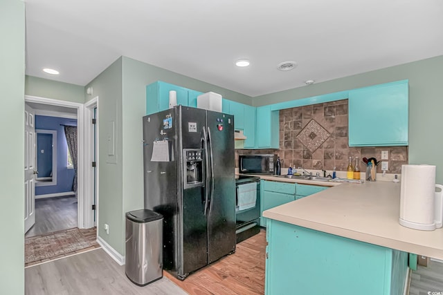 kitchen with black appliances, a peninsula, light wood-style flooring, backsplash, and light countertops