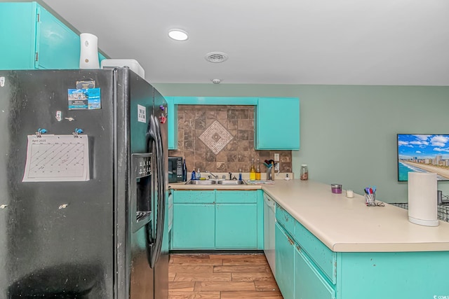 kitchen featuring black appliances, a sink, light wood-style floors, decorative backsplash, and a peninsula