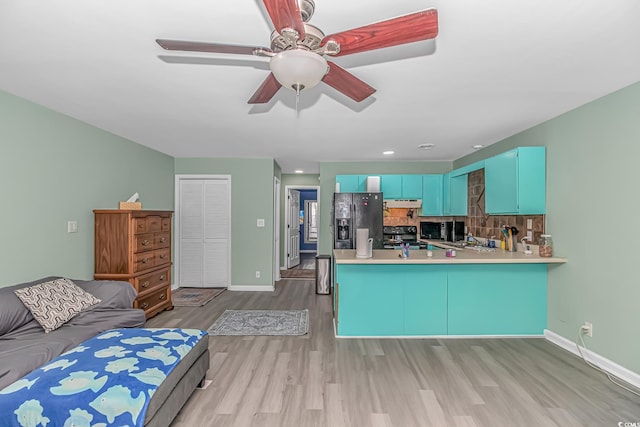 kitchen with black appliances, light wood-type flooring, a ceiling fan, baseboards, and a peninsula
