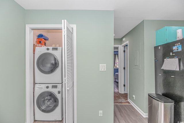 washroom featuring stacked washer / dryer, light wood-style floors, and baseboards