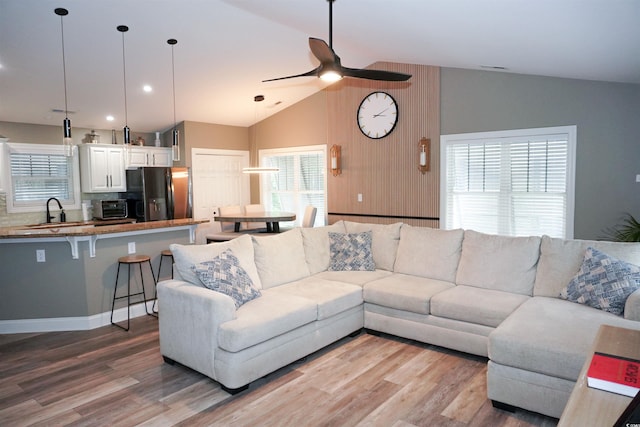 living area featuring lofted ceiling, light wood-style floors, a ceiling fan, and plenty of natural light