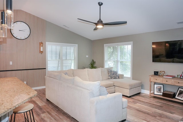 living room with a ceiling fan, light wood-style floors, vaulted ceiling, and baseboards