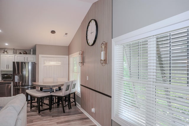 dining area with light wood-type flooring, vaulted ceiling, and baseboards