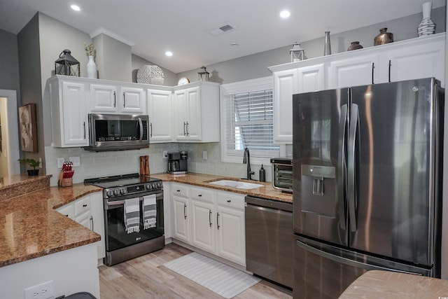 kitchen featuring appliances with stainless steel finishes, a sink, white cabinets, light stone countertops, and backsplash