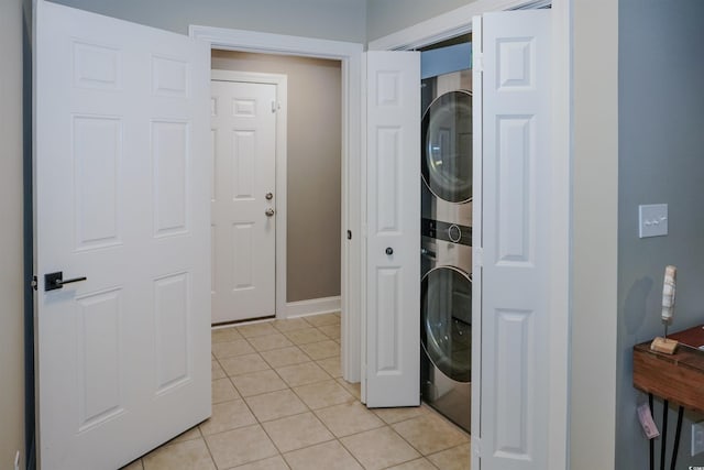 laundry area with stacked washer / drying machine, light tile patterned floors, and baseboards