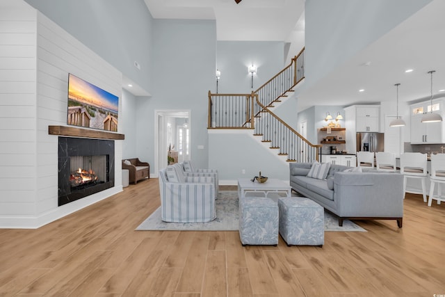 living room with a towering ceiling, a large fireplace, light wood-style floors, and stairway
