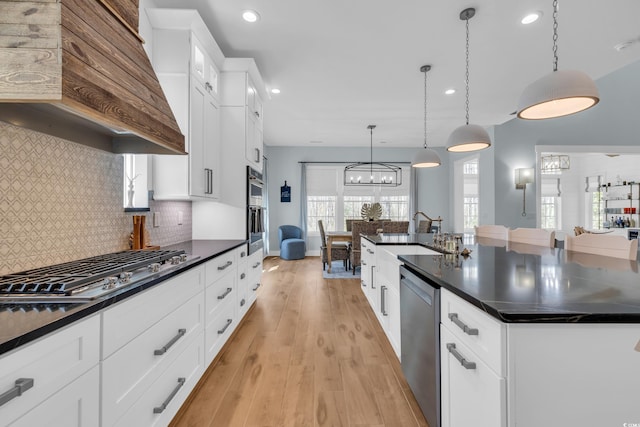 kitchen featuring appliances with stainless steel finishes, a sink, custom exhaust hood, dark countertops, and light wood finished floors