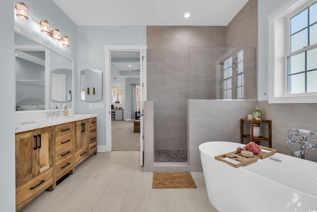 bathroom featuring a freestanding bath, walk in shower, double vanity, healthy amount of natural light, and tile walls