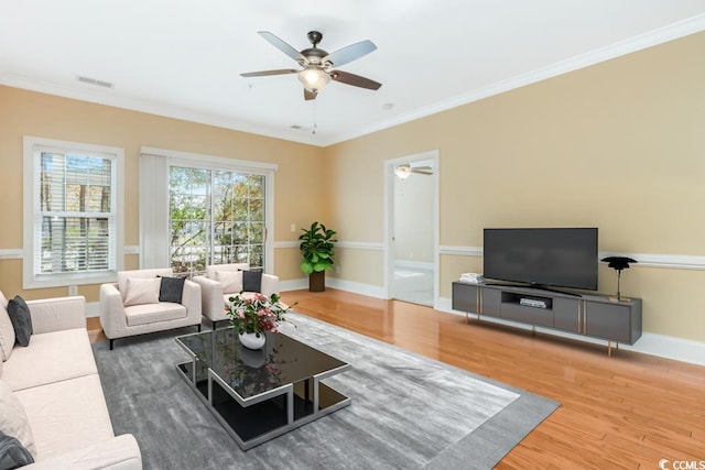 living room featuring ceiling fan, wood finished floors, baseboards, and crown molding