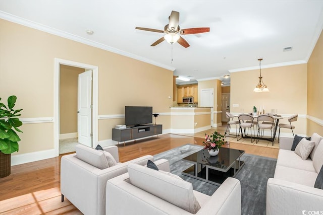 living room featuring ceiling fan, ornamental molding, light wood-style floors, and baseboards