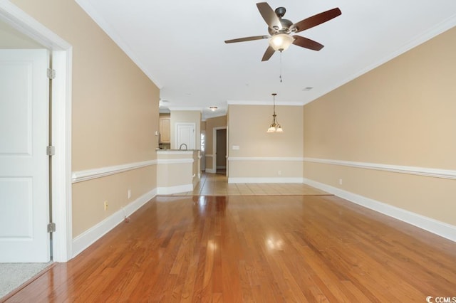 spare room with a ceiling fan, crown molding, light wood-style floors, and baseboards
