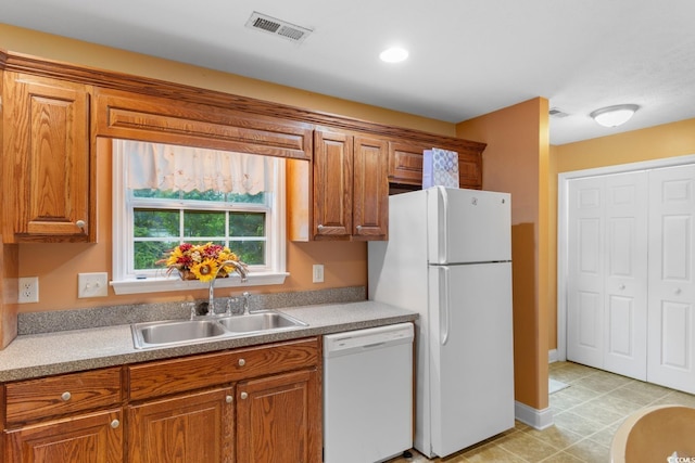 kitchen with white appliances, visible vents, brown cabinetry, and a sink