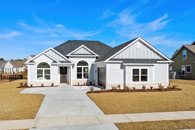 view of front of property with board and batten siding, stone siding, roof with shingles, a front lawn, and driveway