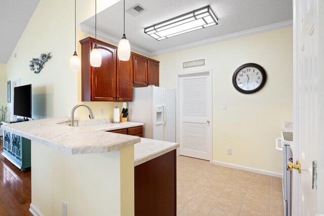 kitchen with a peninsula, white fridge with ice dispenser, crown molding, light countertops, and decorative light fixtures