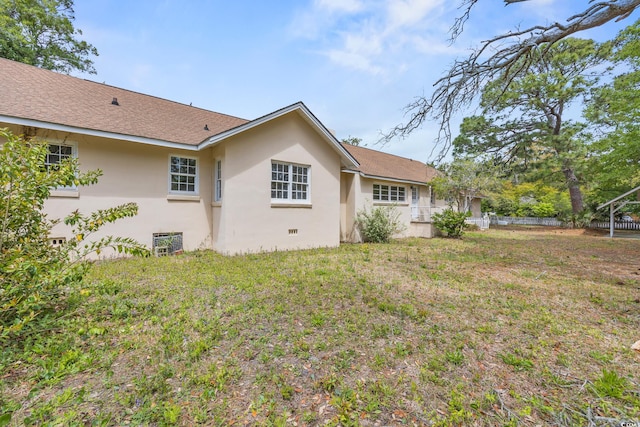 back of house featuring a lawn, stucco siding, and fence