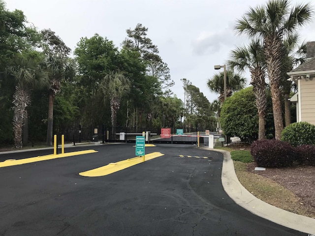 view of street featuring a gate, a gated entry, curbs, and street lights