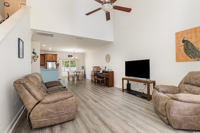 living room featuring ceiling fan with notable chandelier, a high ceiling, light wood finished floors, baseboards, and visible vents