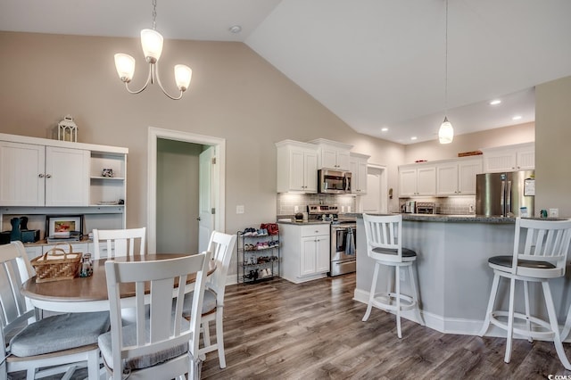 kitchen featuring stainless steel appliances, backsplash, white cabinetry, decorative light fixtures, and a breakfast bar area